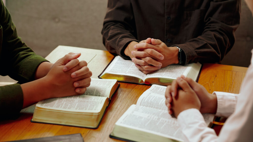 Christian students praying with bibles open on a table